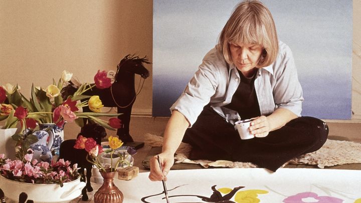 Maija Isola formgav Unikko-mönstret för 60 år sedan, något som uppmärksammas i form av ett jubileum 2024. Här bild som visar Maija Isola sittandes på golvet där hon handmålar ett blomstermönster.