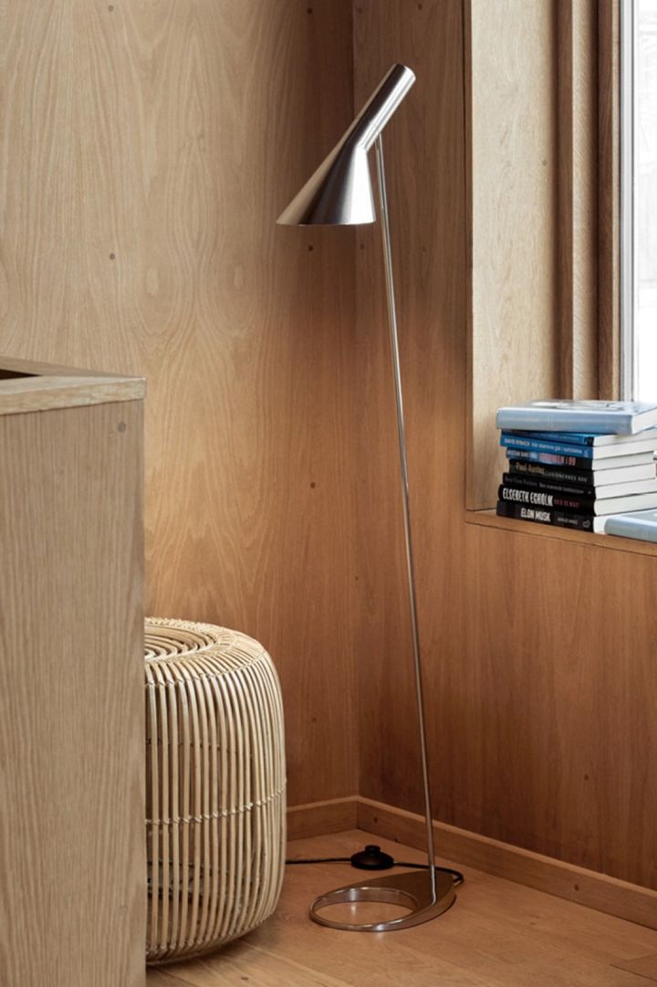 AJ golvlampa från Louis Poulsen, här i rostfritt stål placerad i ett rum med trärena väggar är en populär golvlampa med tidlös design.