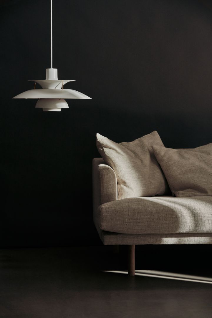 Taklampan PH5 i mononkrom vit från Louis Poulsen, en populär taklampa för vardagsrummet, här bredvid en beige soffa.