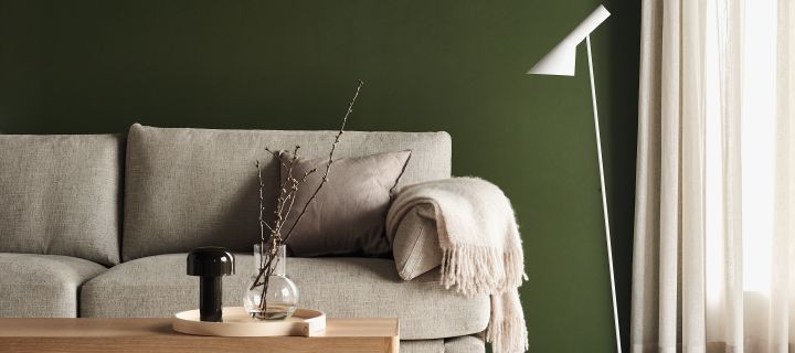 Aj golvlampa i vitt från Louis Poulsen och Bellhop portabel bordslampa i svart från Flos placerade  i grönmålat vardagsrum med beige soffa och soffbord i ljust trä.