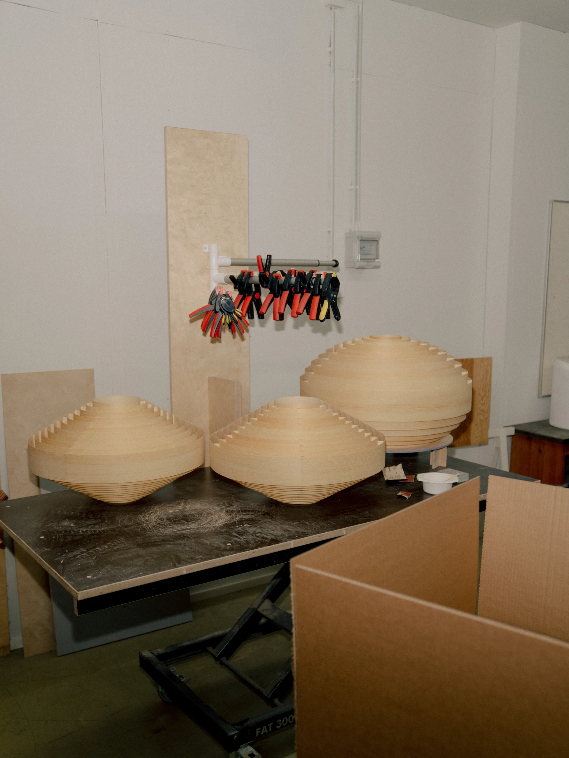 Tre ofärdiga koniska former i ljust skiktat trä på en mörk arbetsbänk i en verkstad.