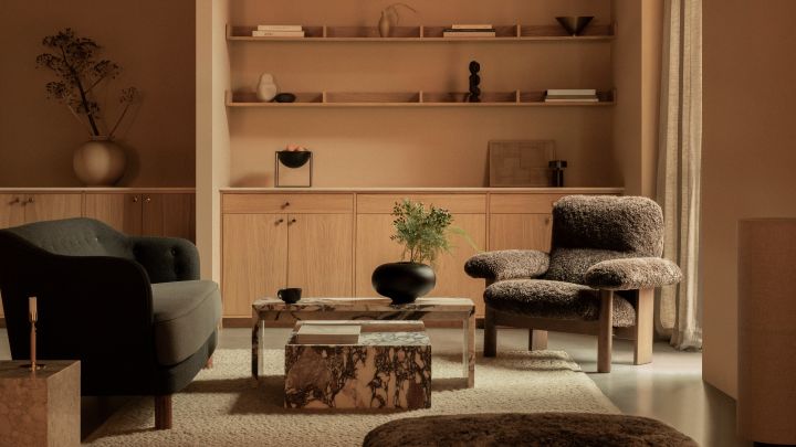 Bild som visar Ingeborg soffa grå textil, Brasilia fåtölj i brunt fårskinn med ekstativ och Plinth soffbord i sten, från Audo Copenhagen.