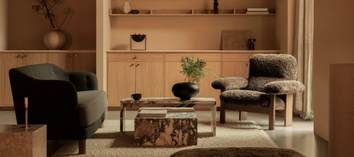 Bild som visar vardagsrumsmiljö med Brasilia fåtölj i brunt fårskinn tillsammans med Ingeborg soffa i grå textil. Mellan bordet står Plinth soffbord i sten, allt från Audo Copenhagen.