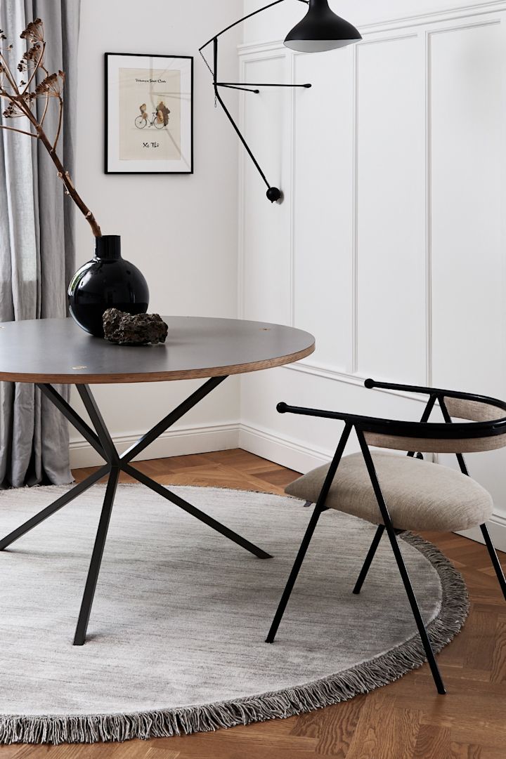 Rund, grå matta i en stilren matplats med detaljer i svart och möber i valnöt. 