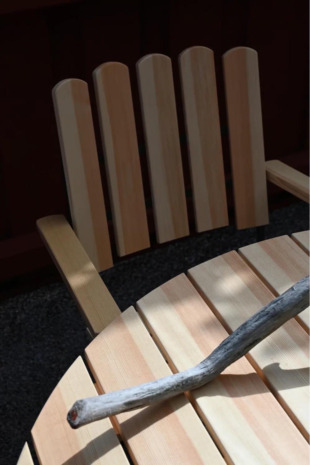 Utemöbler i trä med stolar och ett bord av ljusa trälameller. En bit drivved ligger på bordet, solljus kastar skuggor.