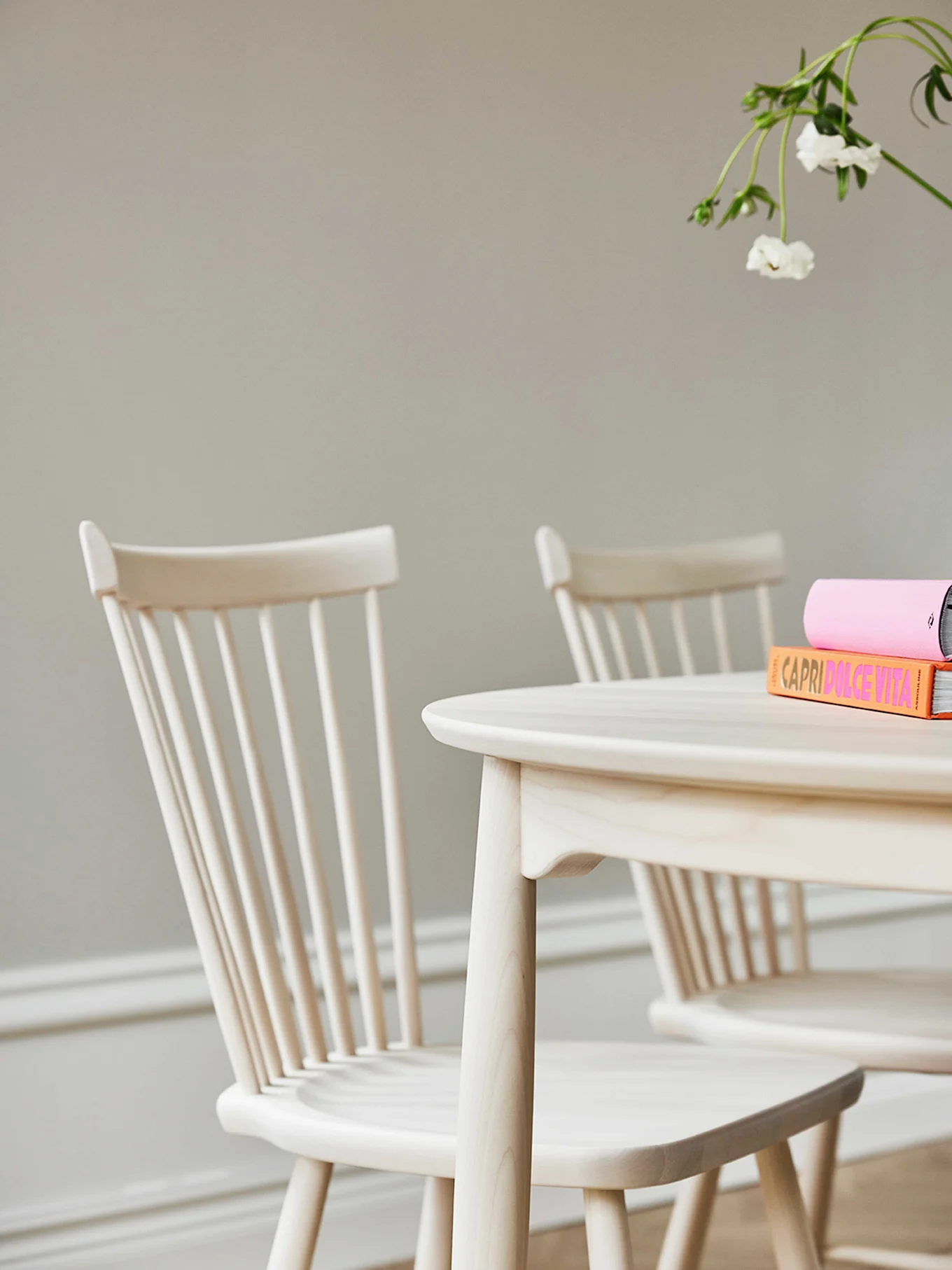 Överblick av ett ovalt matbord i ljust trä med en snidad träskål och tre stolar med mörkbruna sitsar på en brun matta.