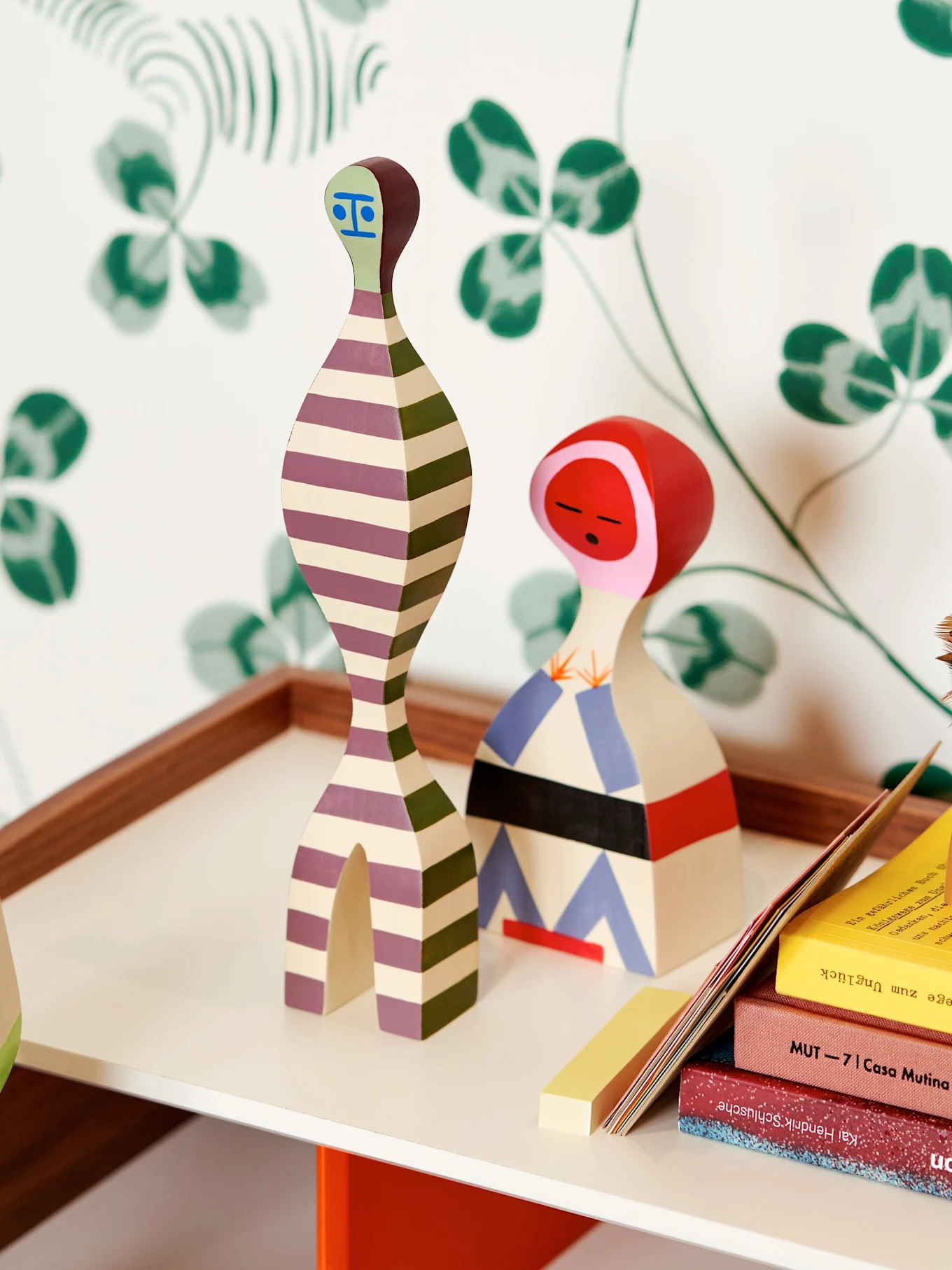 Två abstrakta träfigurer, den ena randig lila/grön, den andra med rött huvud och geometriska mönster.