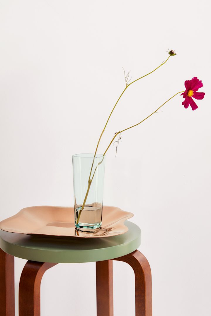 Alvar Aalto vas i ljusgrönt på Alvar Aalto fat i roséguld, placerade på en E60-pall från Artek.