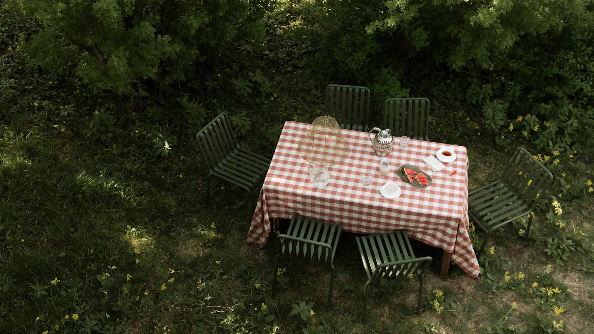 Bild som visar Pallisade utemöbler i form av bord och stolar i grönt från varumärket HAY. Här med en vacker röd- och vitrutig duk på.