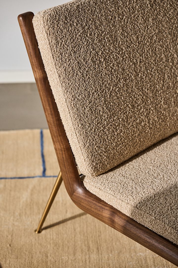 Bild som visar detaljer på Boomerang fåtölj från &Tradition. designad av Hvidt & Møllgaard. Här ser man detaljer i stolsryggen där bakstycket i valnöt möter den textila framsidan i beige.