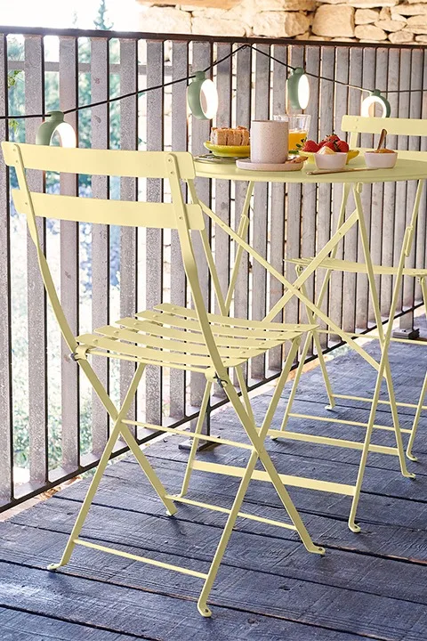 Miljöbild föreställandes bistro cafébord och stolar i pastellgult från Fermob ståendes på terass i trä.