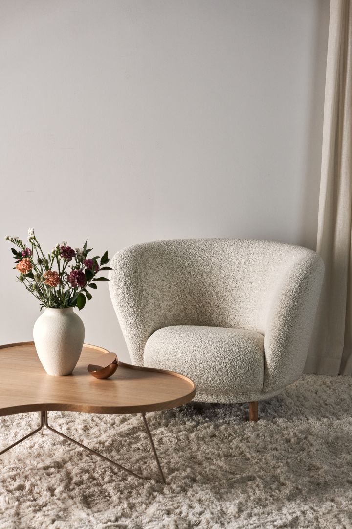Bild som visar det klassiska Flower soffbord från Swedese, här i vitpigmenterad ek placerat på en ljus fluffig matta med en vit fårskinnsfåtölj bredvid.