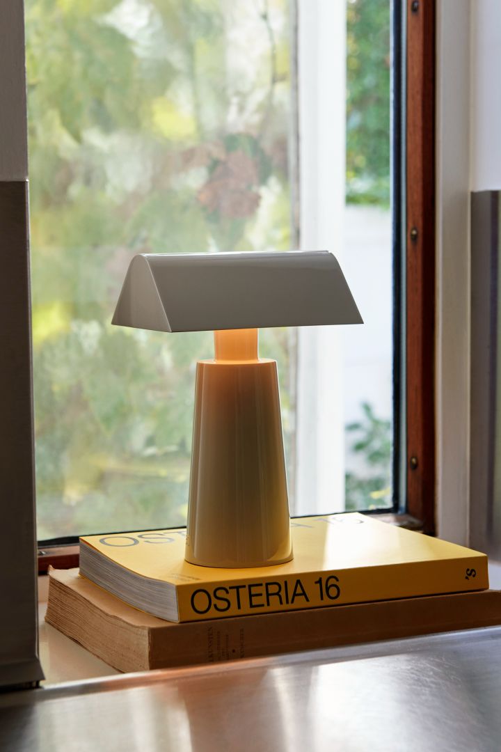 Inred med lampor i fönster med exempelvis en portabel lampa som Caret MF1 i färgen silk grey från &tradition, här placerad på böcker i ett djupt fönster.