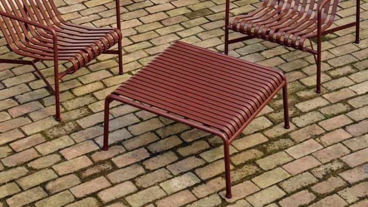 BIld som visar Pallisade loungebord i färgen iron red från danska HAY. Bordet står tillsammans med två Pallisade loungestolar i samma färg på tegelgolv.