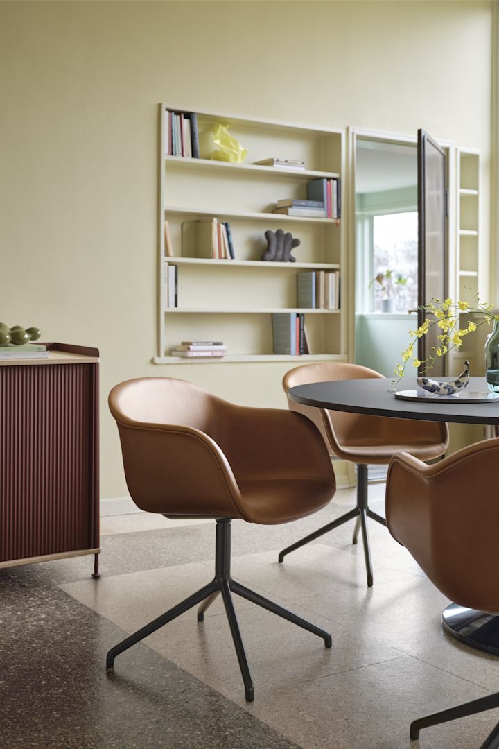 Bild som visar Fiber Chair kontorsstol från Muuto med svart underrede och sits i cognac placerad kring ett runt bord i svart.