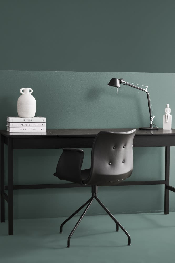 Grönt hemmakontor med svart arbetsstol och svart bordslampa och svart skrivbord. 