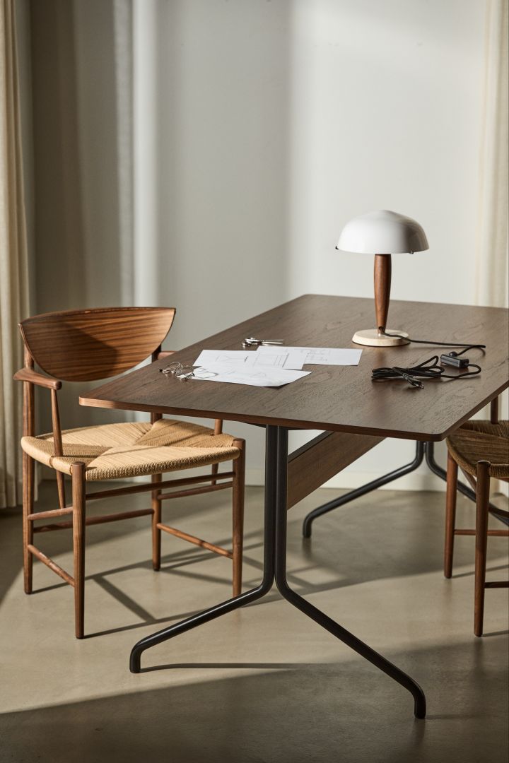 Bild som visar Pavilion matbord i valnöt tillsammans med Herman bordslampa, vid bordet står en Drawn stol i valnöt med flätad sits.