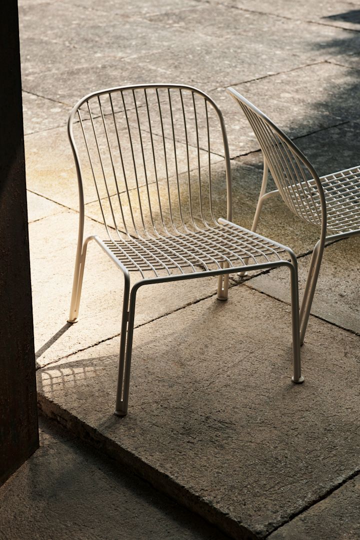 Bild som visar Thorvald loungestol i den vita färgen ivory från &Tradition.. Stolen står placerad på stenlagt uteplats.