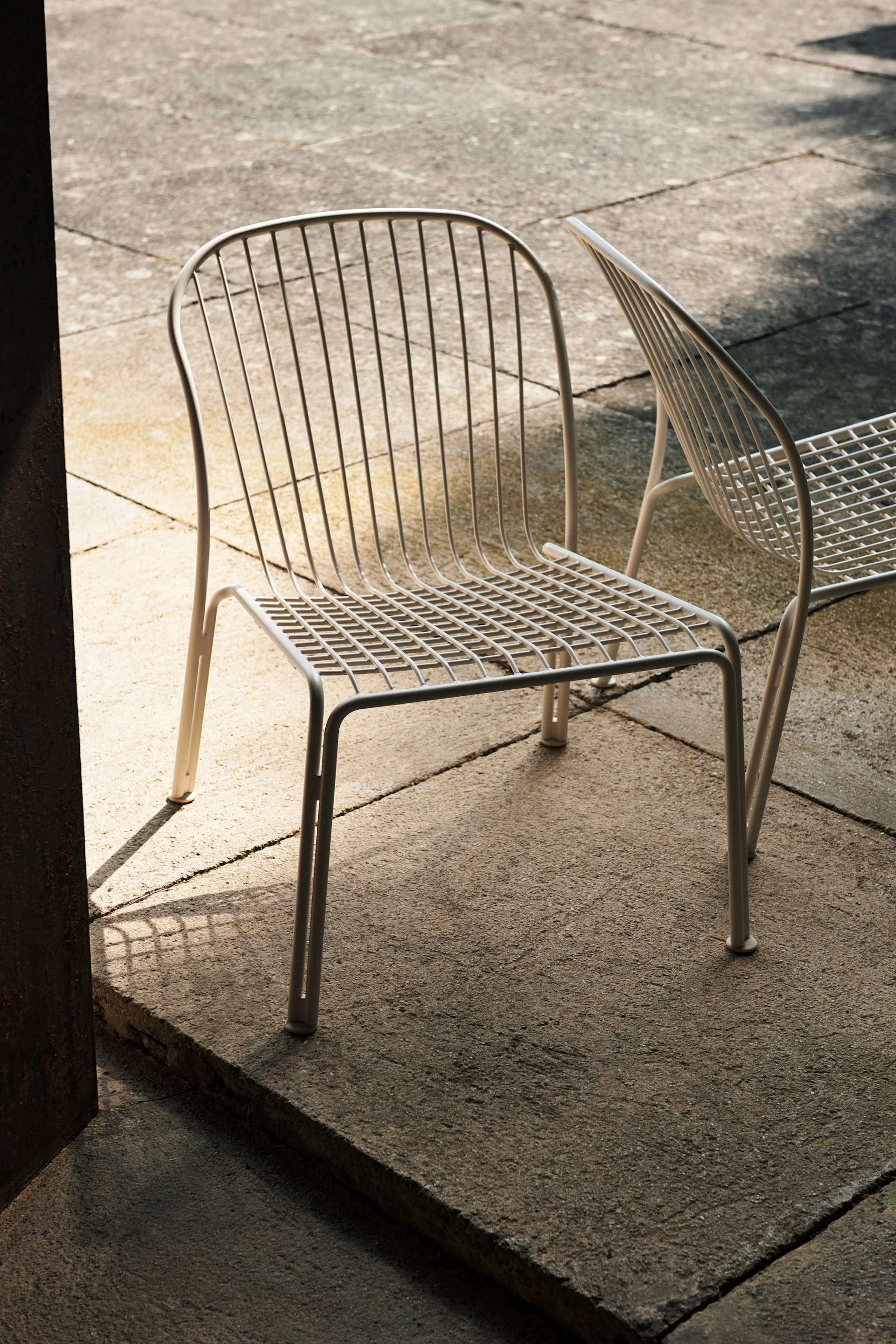 Bild som visar Thorvald loungestol i den vita färgen ivory från &Tradition.. Stolen står placerad på stenlagt uteplats.