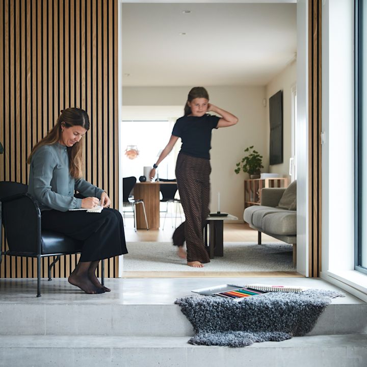 Hemma hos familjen Moser är det inrett i en mix av klassiskt och modernt. I den stora hallen tronar en trappa i betong och väggarna är klädda i trendig träpanel. Här står en Bruno-fåtölj från Källemo och i trappan ligger ett mjukt fårskinn i grått.