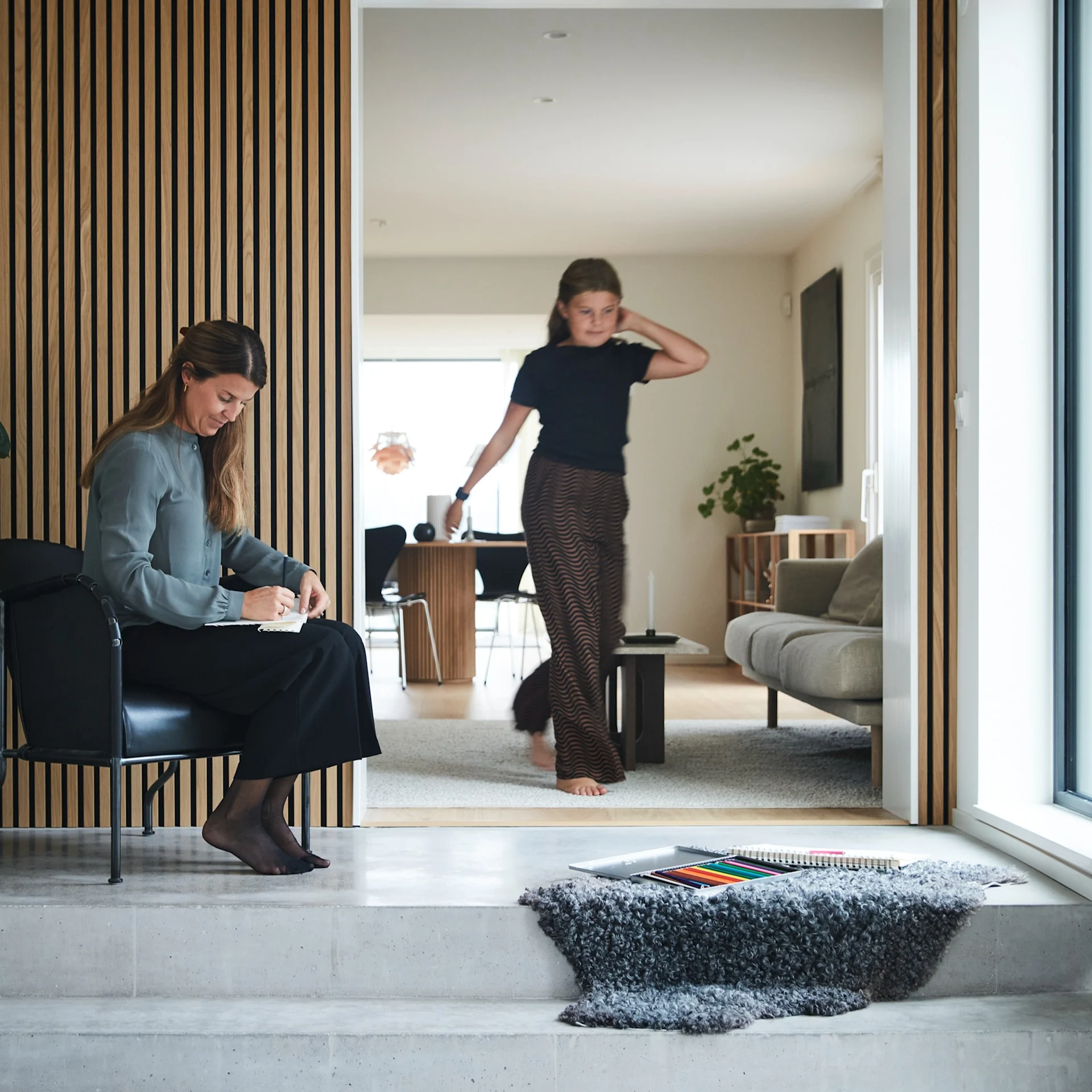 Hemma hos familjen Moser är det inrett i en mix av klassiskt och modernt. I den stora hallen tronar en trappa i betong och väggarna är klädda i trendig träpanel. Här står en Bruno-fåtölj från Källemo och i trappan ligger ett mjukt fårskinn i grått.