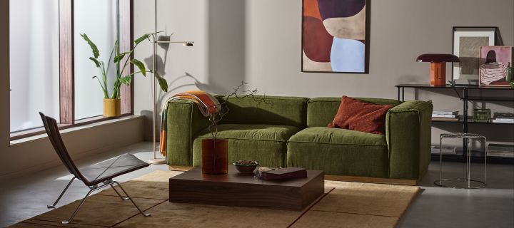 Bergsdal soffa i grönt från 1898 är perfekt att inreda med för ett snyggt vardagsrum. Här i vardagsrumsmiljö med tavlor, textilier och belysning i varma, jordnära toner.