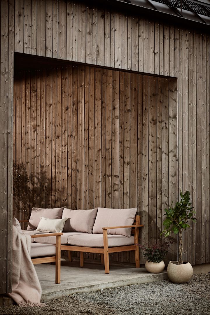 Bland sköna loungemöbler är Stockaryd soffa från 1898 en väl värdig kandidat. Soffan som är tillverkad i teak köps med tillhörande dynor, här stående på uteplats med dynor i beige.