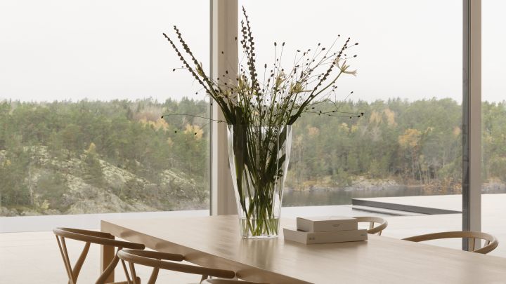 Bild som visar Reed vas i klarglas 50 cm från Orrefors placerad på köksbord i trä, vasen är fylld med gröna strån och enkla kvistar.
