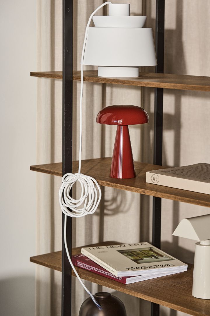 Bild som visar Como portabel lampa i färgen burgundy tillsammans med Utzon lampa i vitt, placerade på hylla i ek.