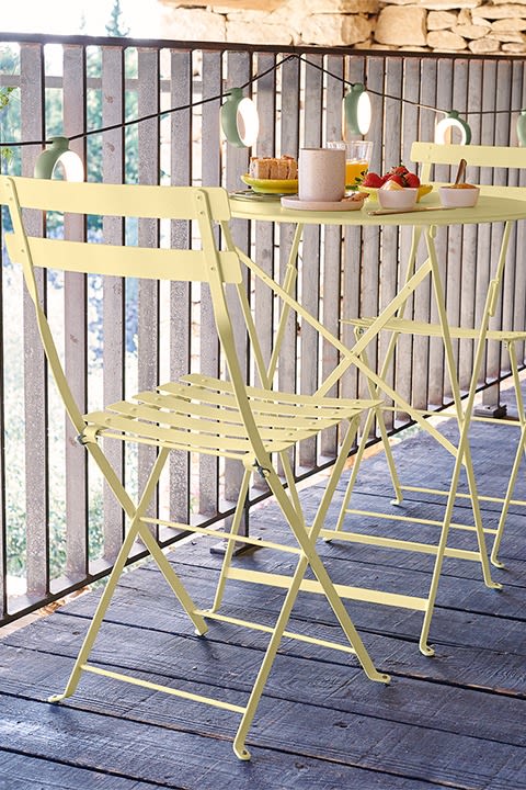 Miljöbild föreställandes bistro cafébord och stolar i pastellgult från Fermob ståendes på terass i trä.