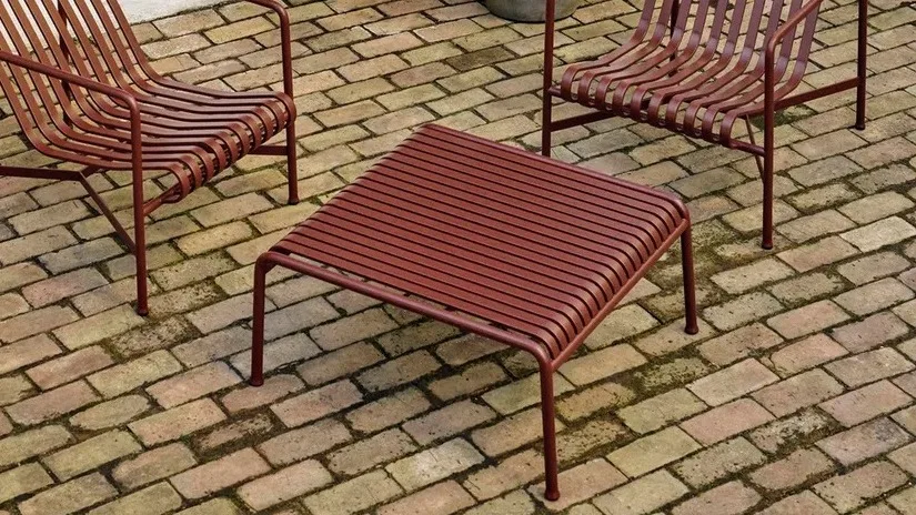 BIld som visar Pallisade loungebord i färgen iron red från danska HAY. Bordet står tillsammans med två Pallisade loungestolar i samma färg på tegelgolv.