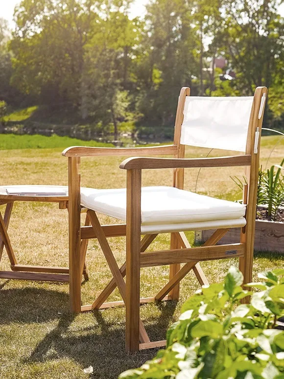 Regissörstol i teak med vitt tyg och dyna, bredvid ett matchande litet bord utomhus i en trädgård.
