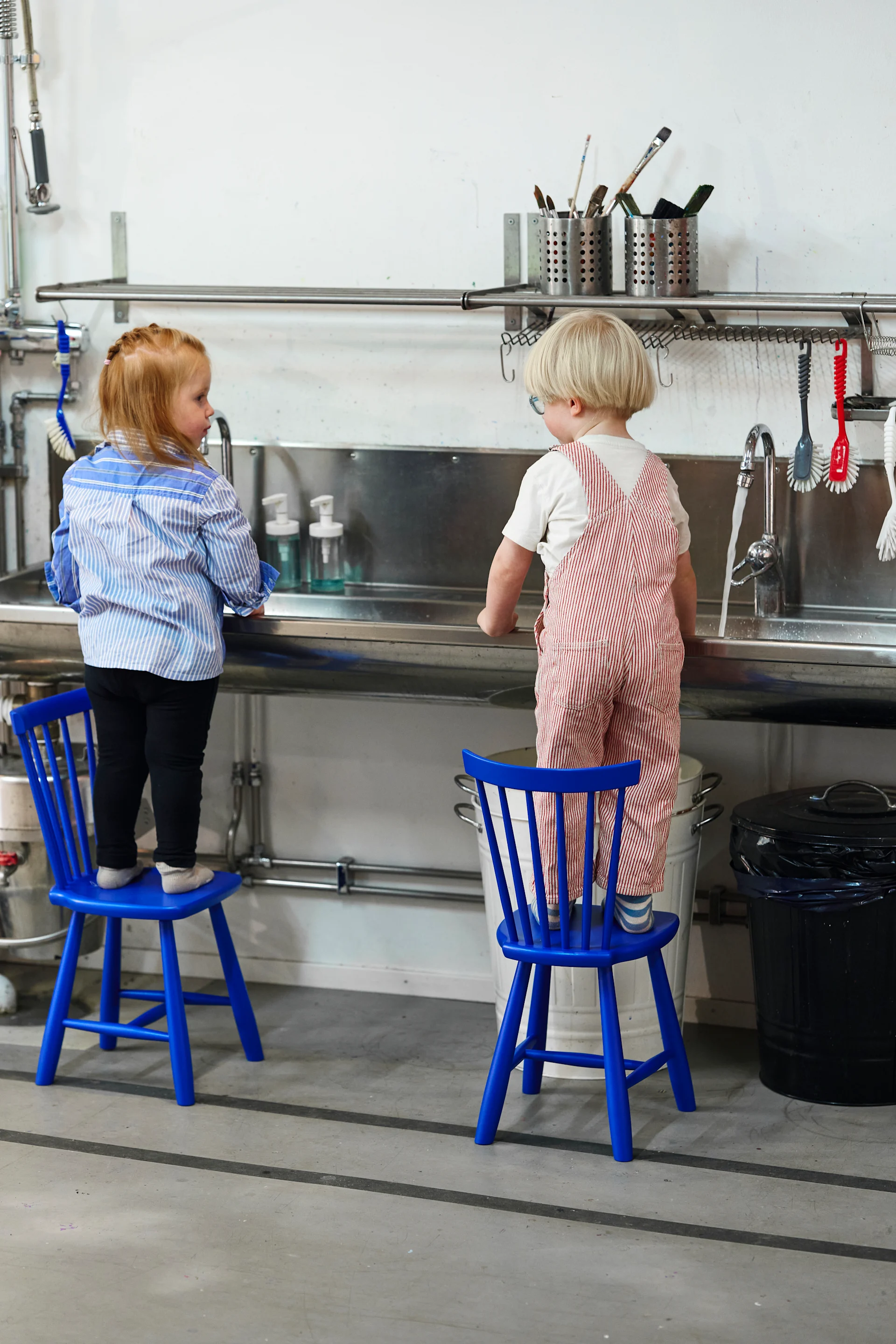 Tips på julklappar - Lilla Åland barnstol i koboltblått från Swedese. Här i ett industriellt kök med två barn stående på varsin stol., 