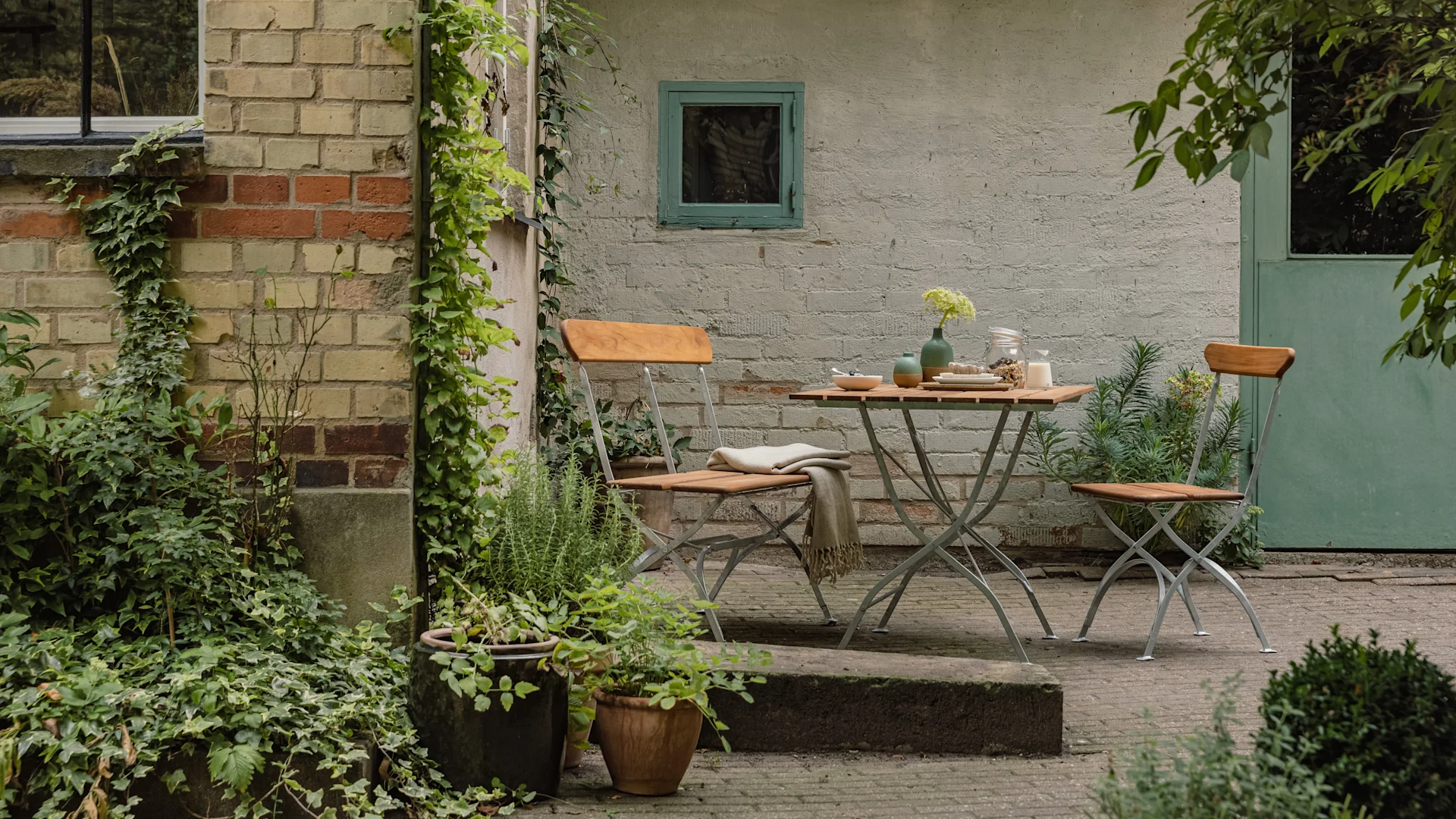 Bryggeriserien från Grythyttan Stålmöbler, här i teak placerad på en stenlagd uteplats.