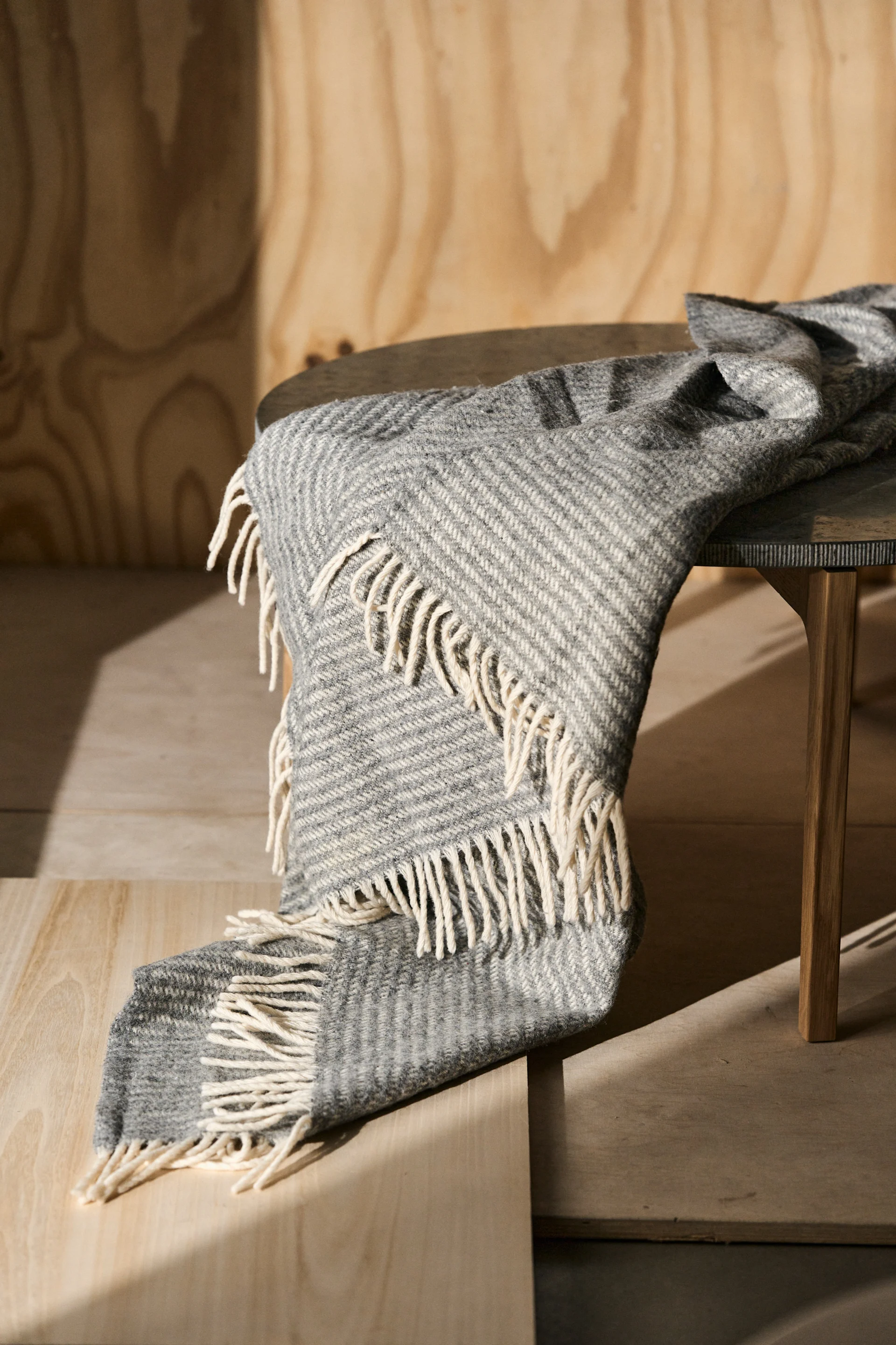 Ralph ullpläd i grått från Klippan Yllefabrik, hängandes över ett bord.