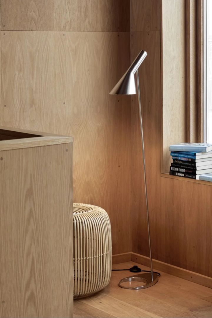 AJ Golvlampa i rostfritt stål från Louis Poulsen är en klassiker bland snygga golvlampor, formgiven av Arne Jacobsen 1960., Här placerad vid läshörna i modern miljö med träpaneler på väggarna.