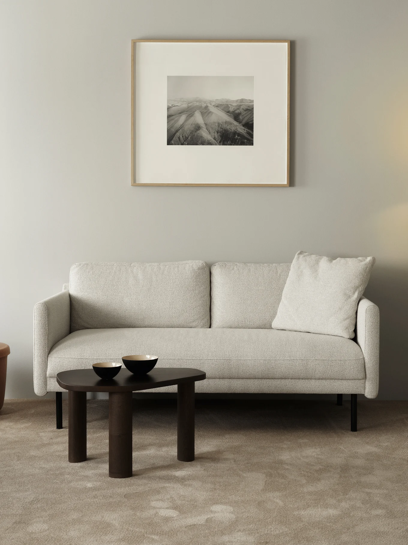 Ljus texturerad soffa, mörkt organiskt soffbord med två guldkantade skålar, inramad svartvit bergskonst.