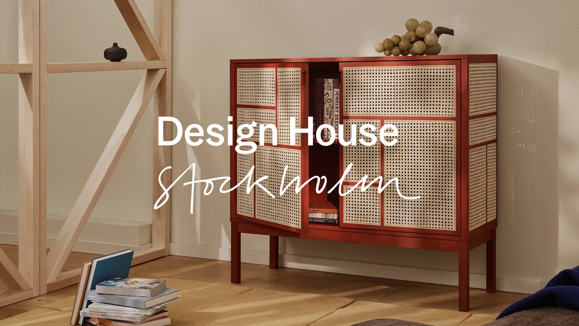 Texten Design House Stockholm över ett träbord med modernt vitt porslin, gul frukt och blommor, mot en ljus trävägg.