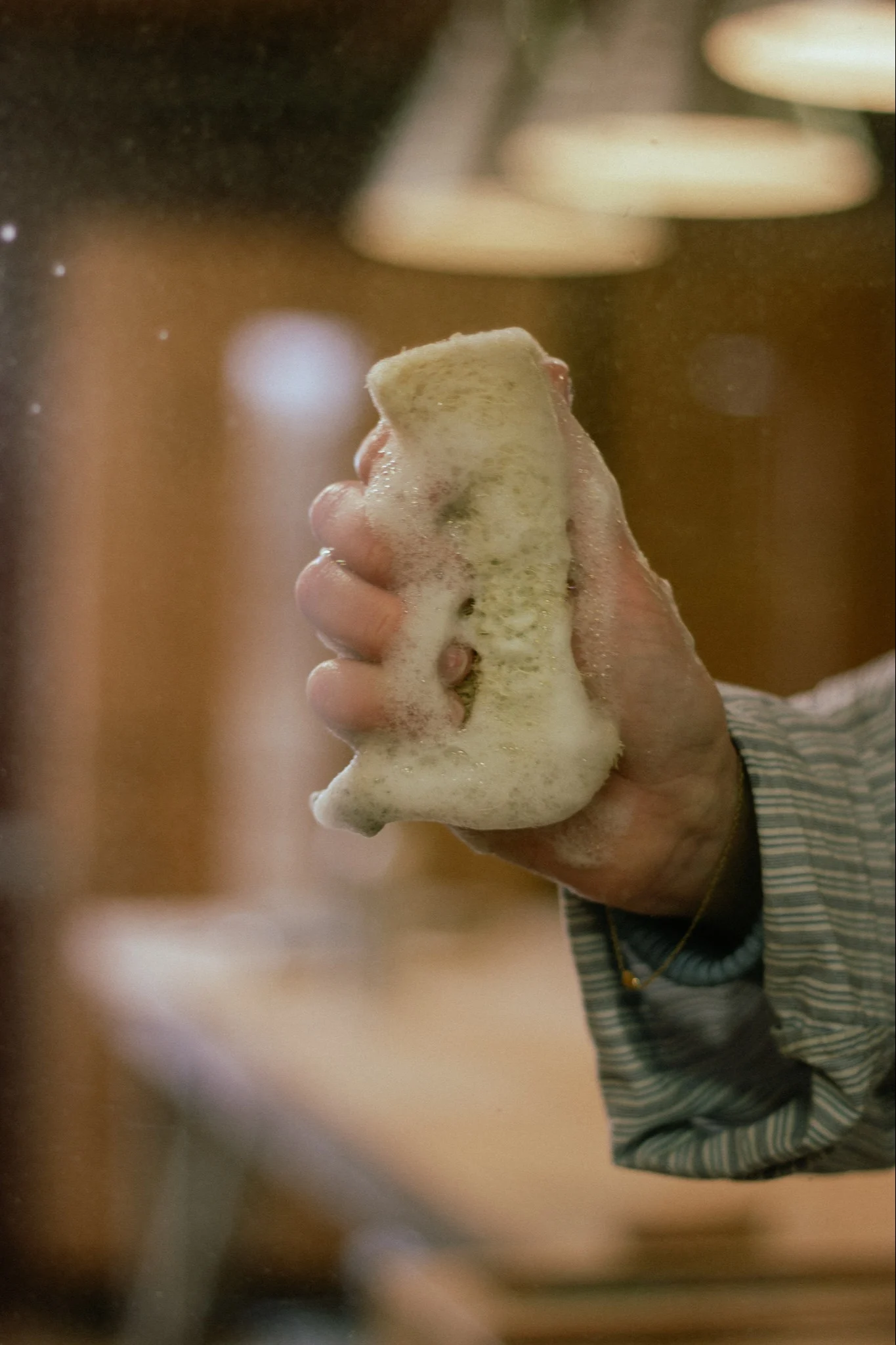 Hand håller en skummig svamp med en randig skjortärm synlig.