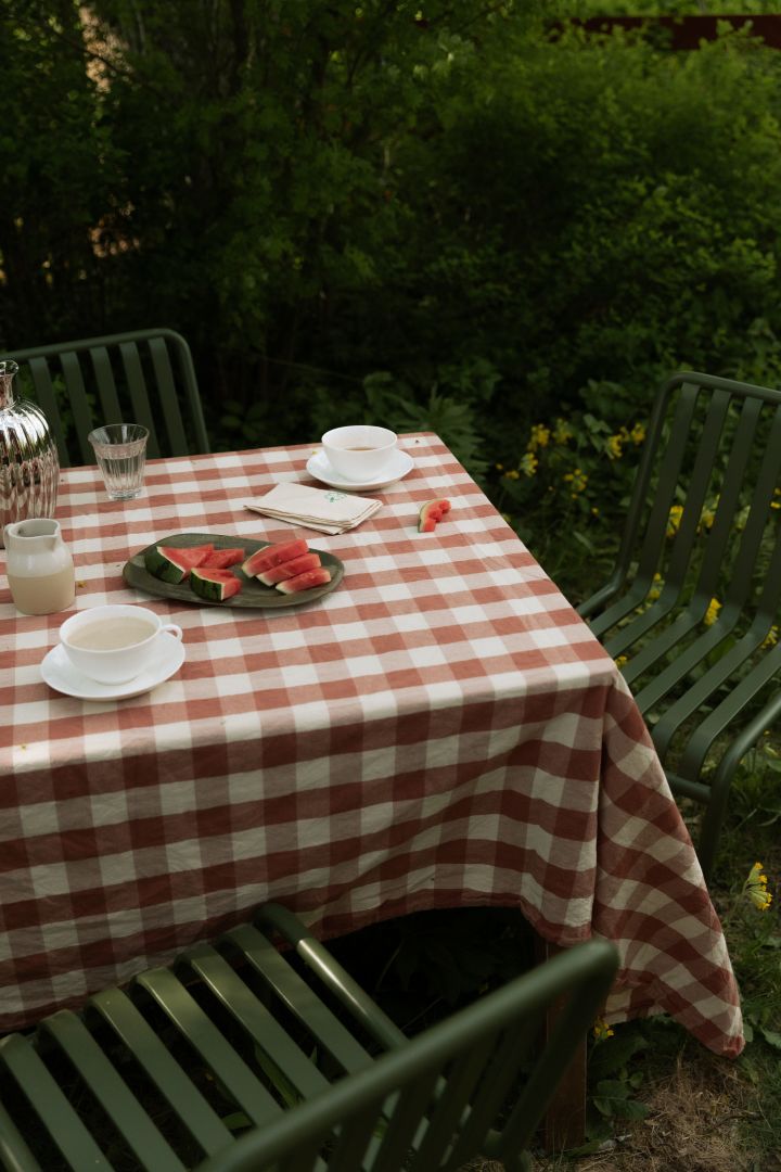 Bild som visar Pallisade bord och stol i grönt från HAY, placerat utomhus i gräs. På bordet ligger en röd- och vitrutig duk.