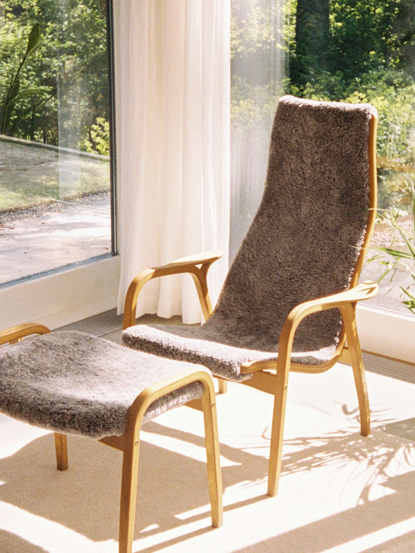 Högryggad fåtölj med brunt fårskinn och elefantkudde, matchande fotpall och sfärisk papperslampa.