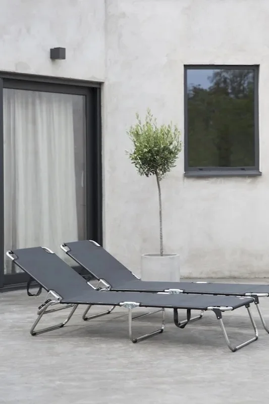 Bild som visar två Amigo solstolar i grått, ståendes på uteplats framför ett hus med ett olivträd bredvid.