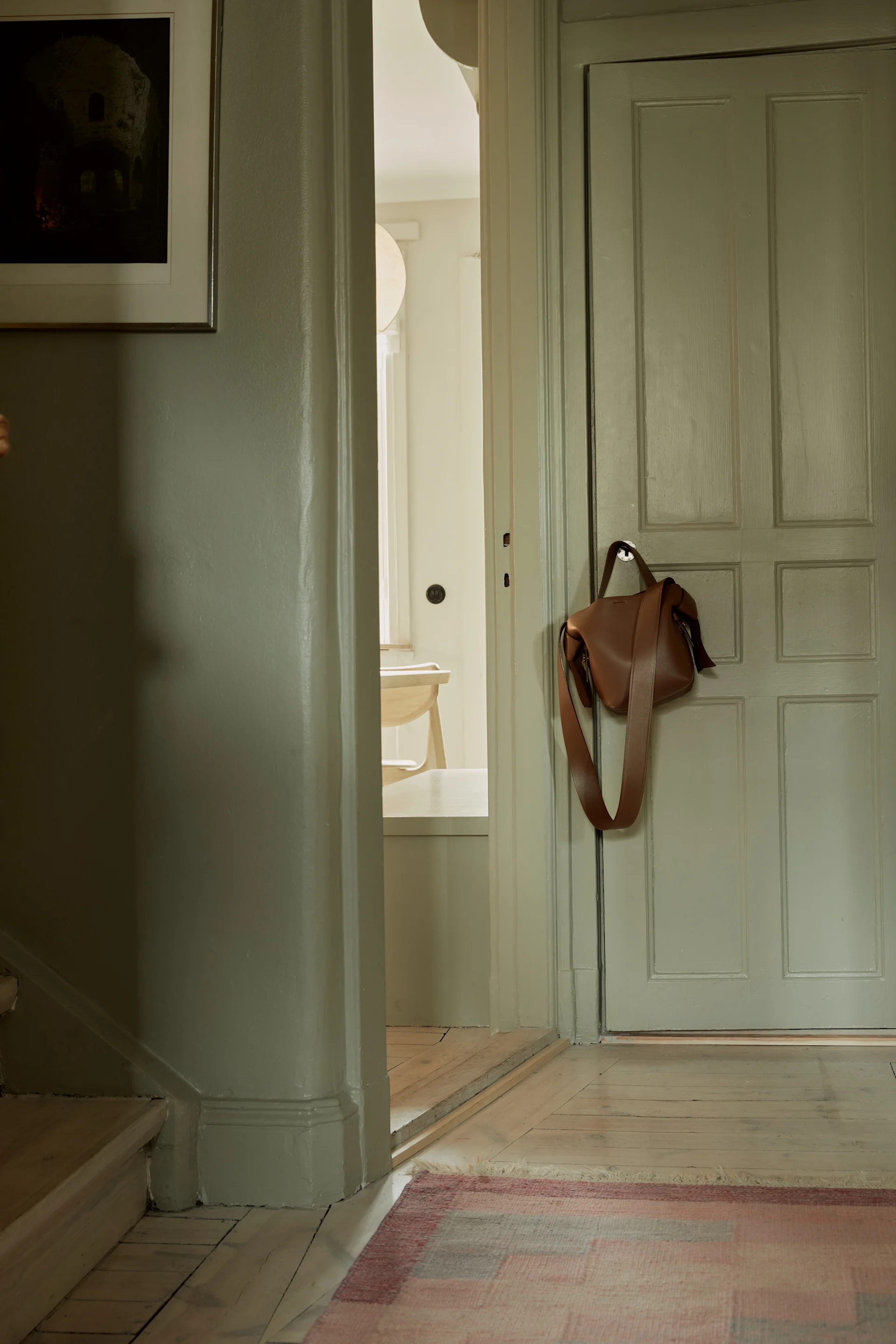 En monokrom grön hall med en brun läderväska hängande på ett dörrhandtag.
