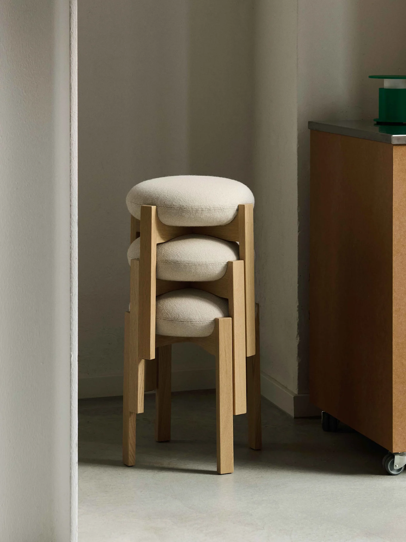 Tre staplade pallar med ljusa träben och runda, ljusa klädda sitsar i ett hörn.