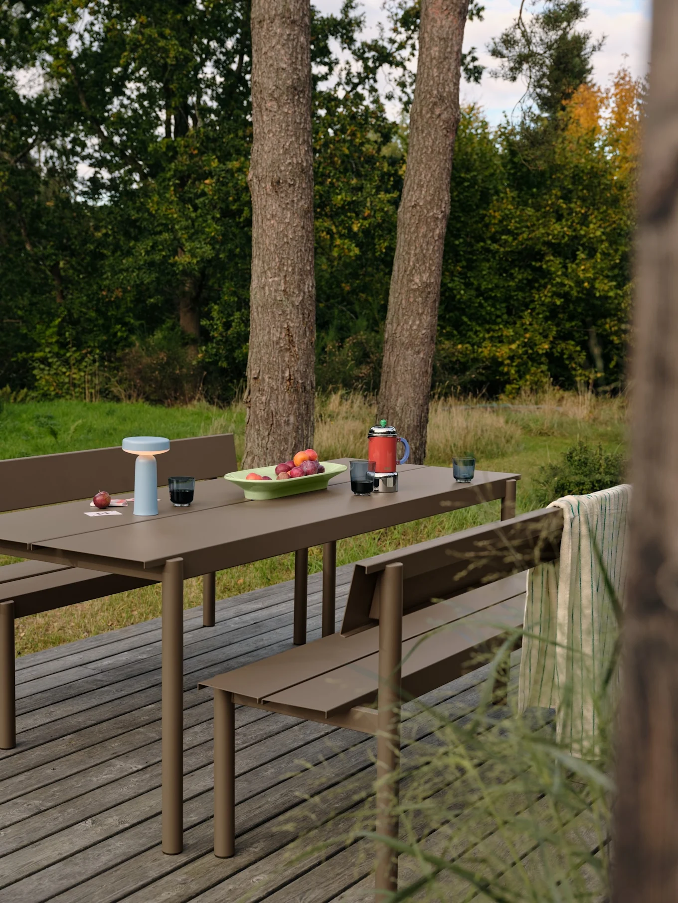 Utepicknickbord med ljusblå lampa, frukt och röd termos på en träaltan.