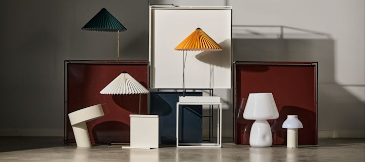 Bild som visar Tray table sidobord i rött och vitt, på och framför står Matin-lampor i olika färger placerade tillsammans med en Apollo-lampa och portabel PC-lampa, samtliga produkter från varumärket HAY.