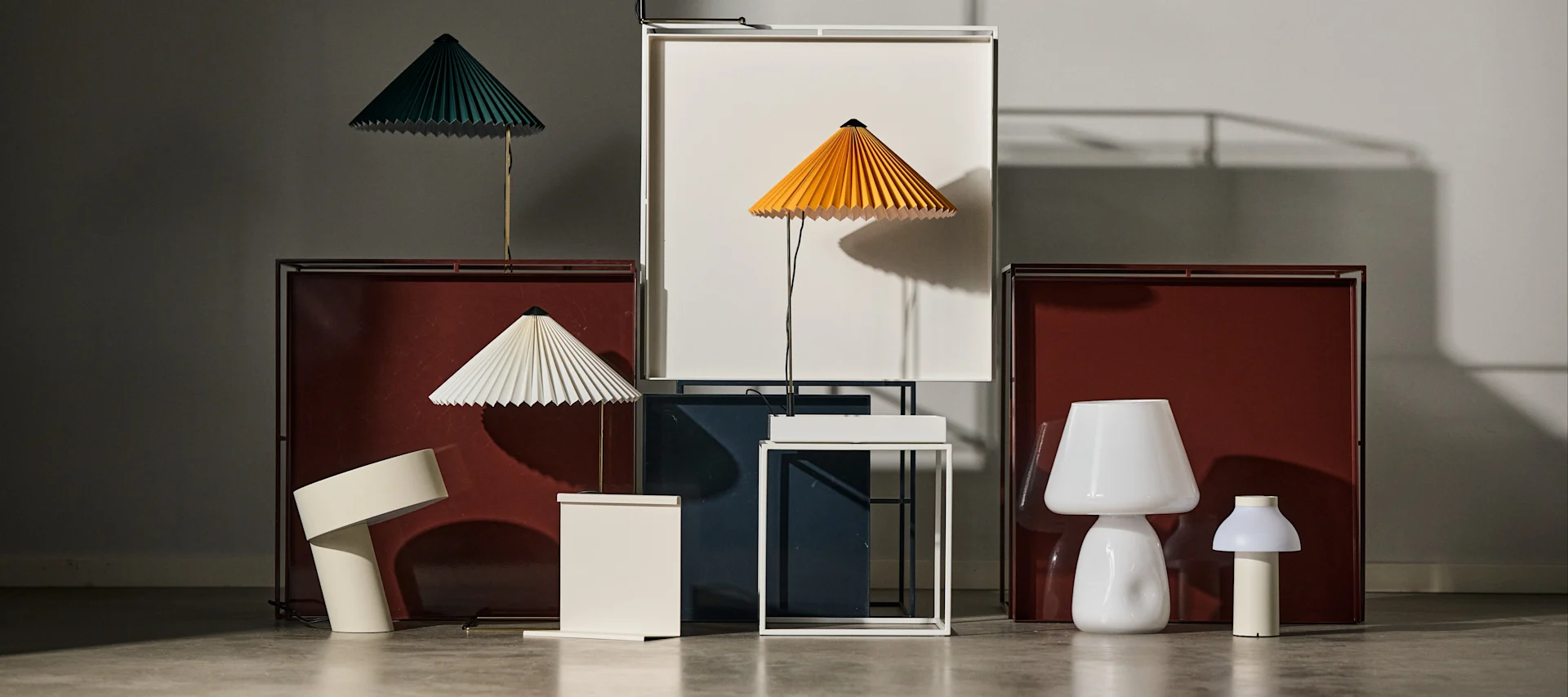 Bild som visar Tray table sidobord i rött och vitt, på och framför står Matin-lampor i olika färger placerade tillsammans med en Apollo-lampa och portabel PC-lampa, samtliga produkter från varumärket HAY.