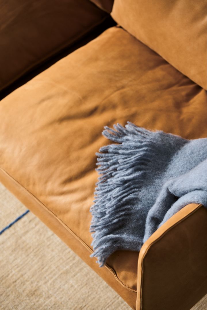 Rengör soffa i läder, som Tiki soffa från Fogia, här i cognacsbrunt med en ljusblå pläd över armstödet.