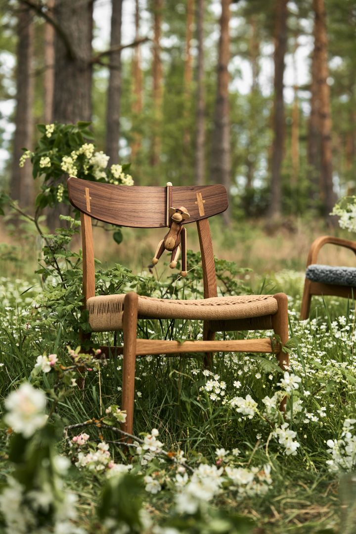 Bild som visar CH23 stol i valnöt med naturflätad sits, här placerad i blommande skogsdunge.
