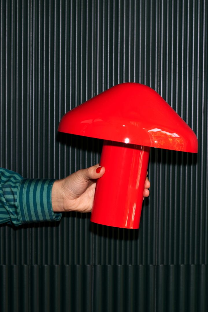 Pao portabel bordslampa från Hay i en härlig röd nyans. här placerad i en hand. En populär bordslampa i portabelt format som gör den enkel att flytta runt.